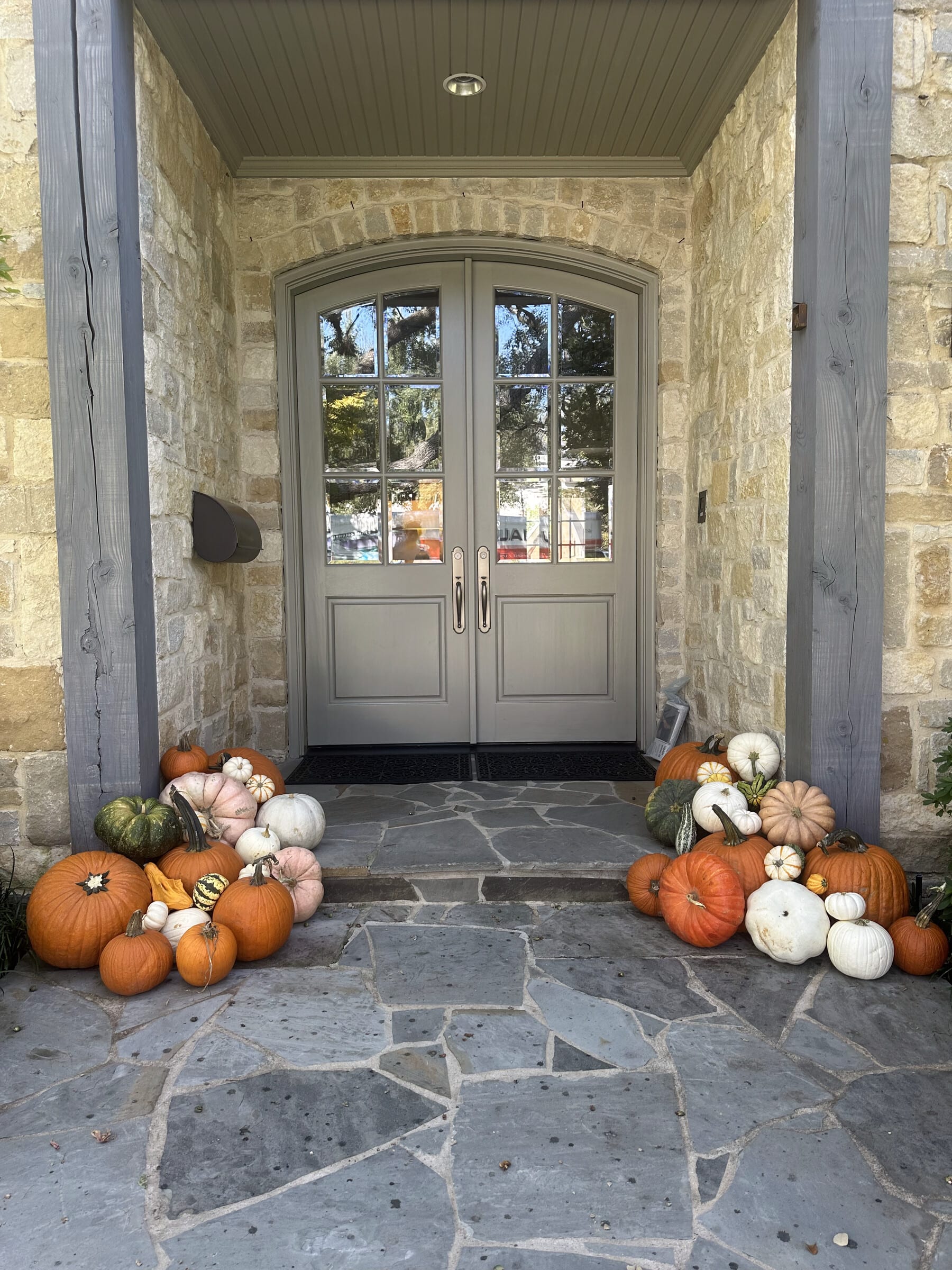 Pumpkins and gourds banked on both sides of arched double doors at a stone home with a flagstone entry