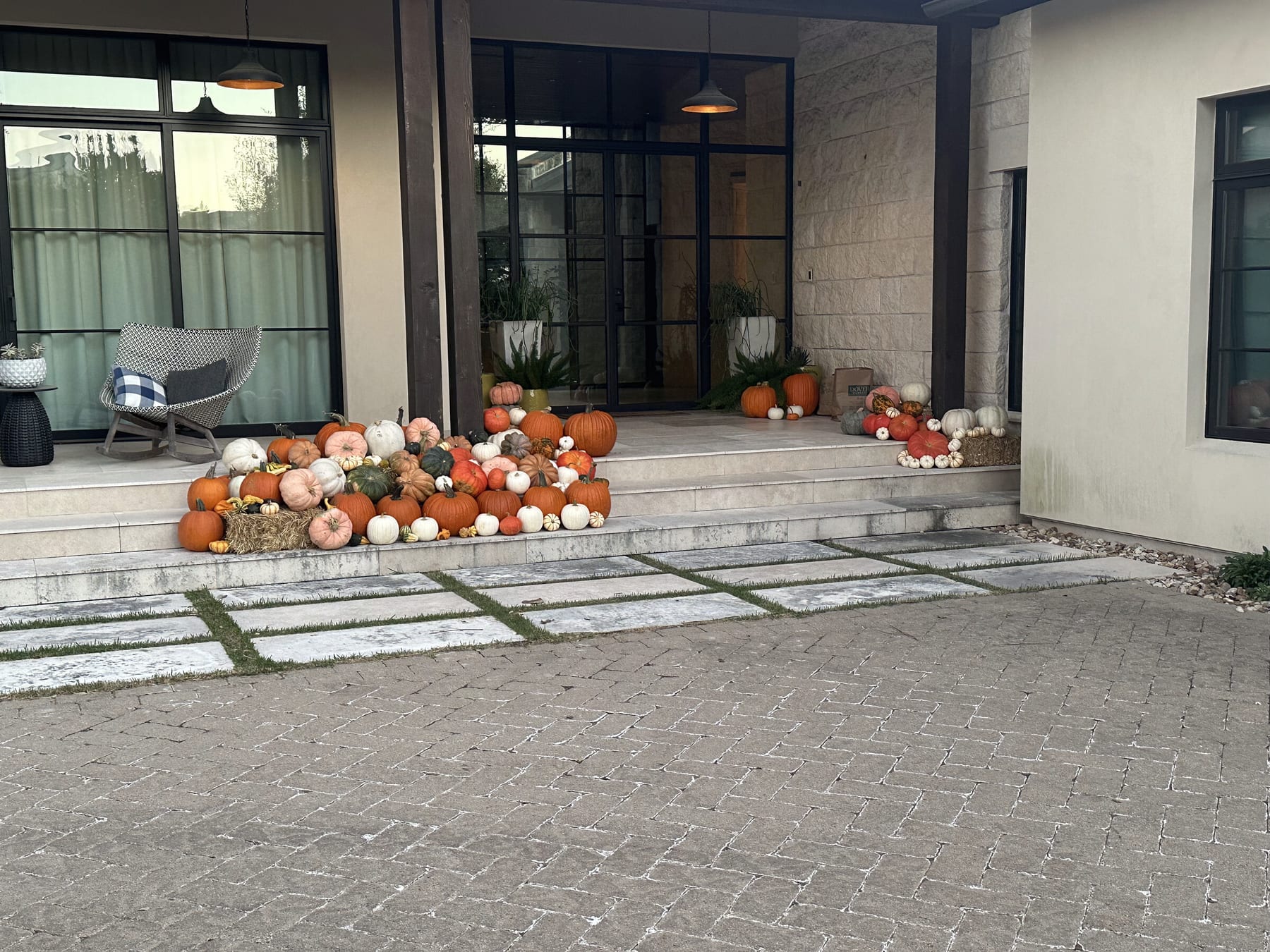 Pumpkins lining the entry steps of a modern home with black steel windows and a paver drive